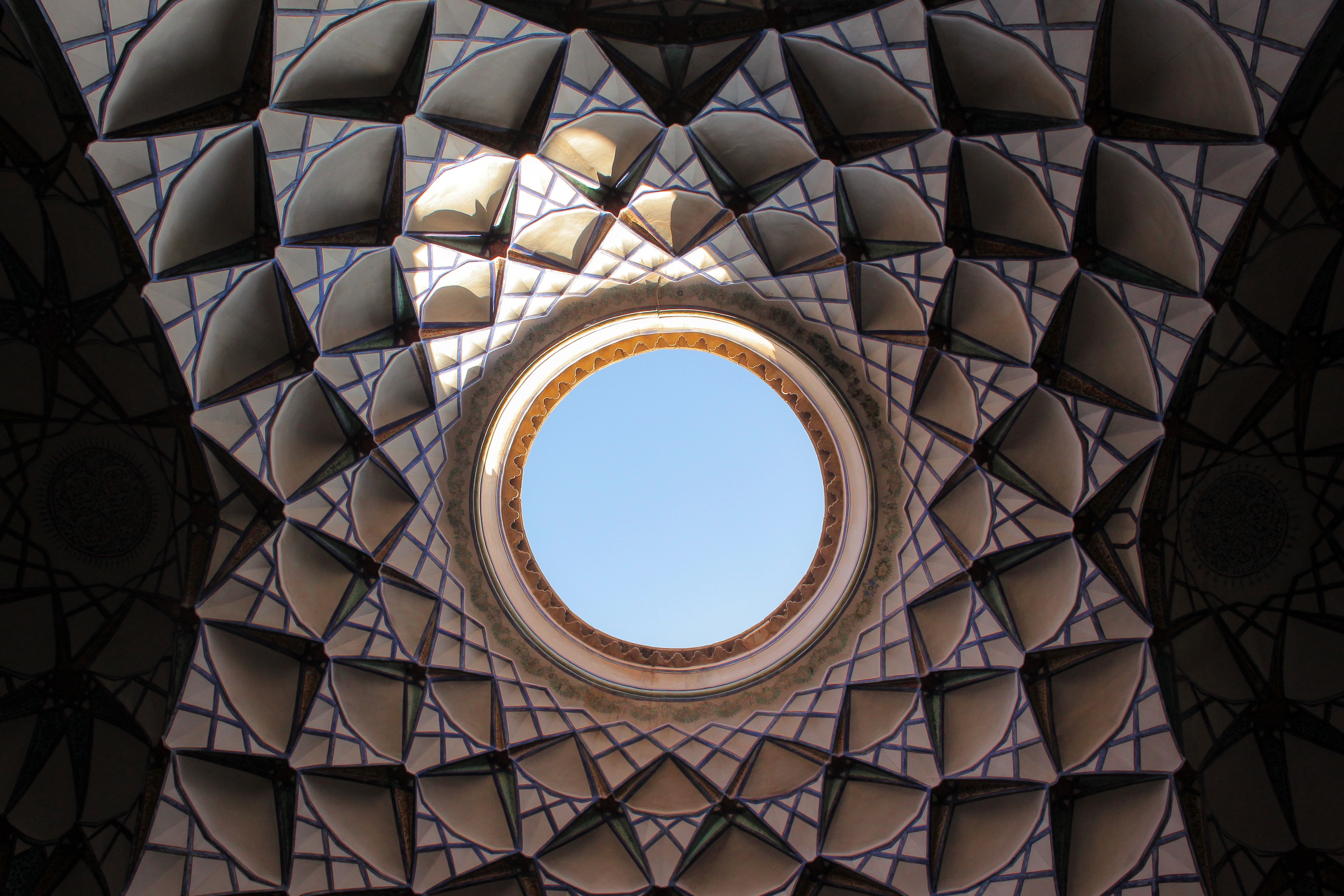 Upward view of the sky through a circular opening in an ornate ceiling