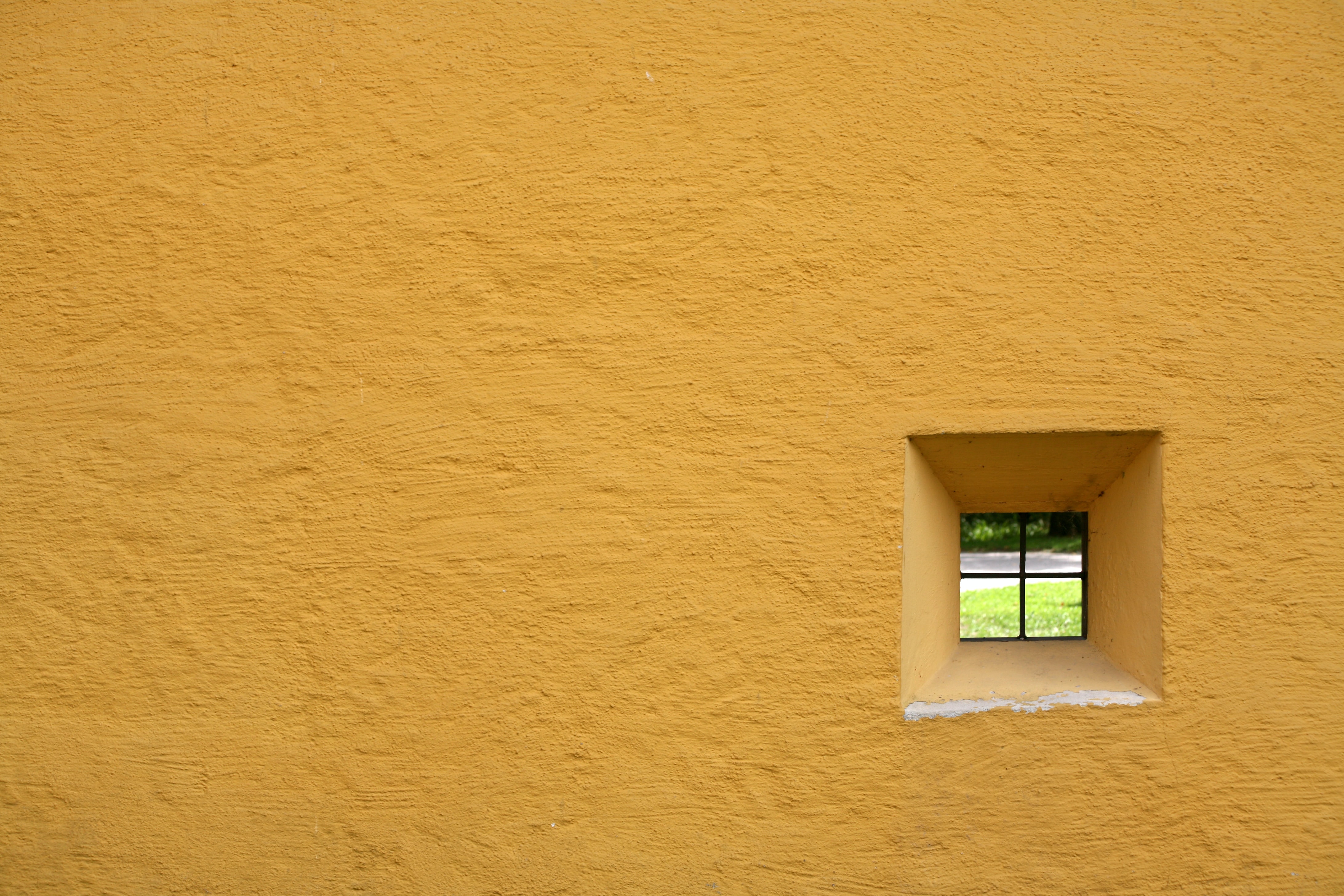 A yellow wall with a tiny window in the lower right
